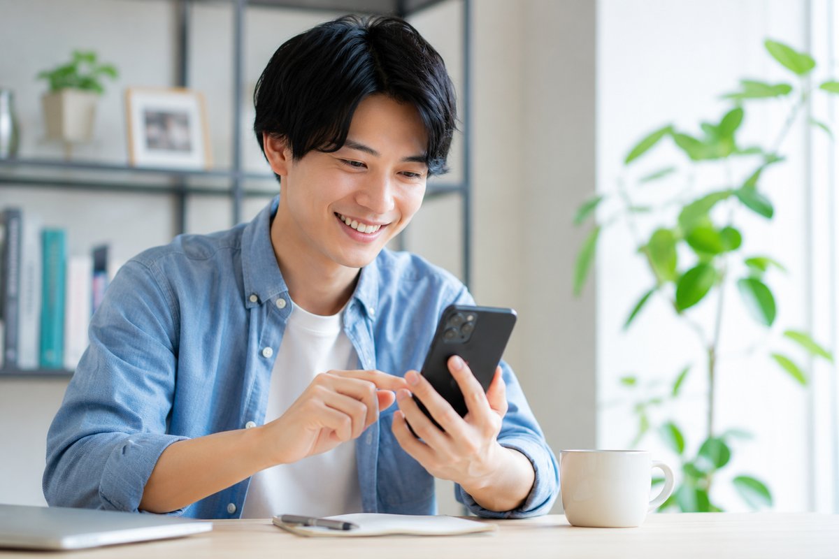スマートフォンを持って笑顔の男性。スマホ代節約成功のイメージ