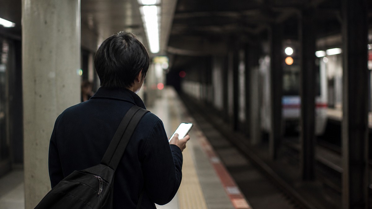 地下鉄の駅構内でスマートフォンの電波状況を確認する人
