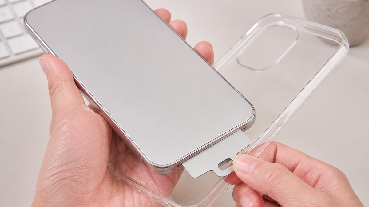 スマホケースと本体の間に薄いストラップホルダーのシートを挟み込む手元