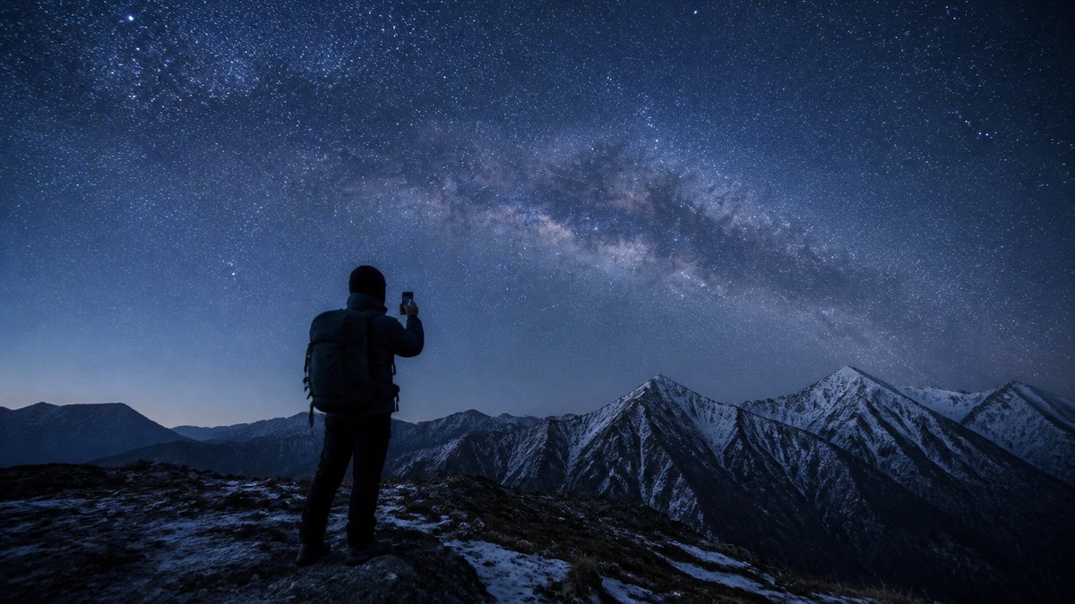 星空の下でスマートフォンを手にする登山者のシルエット